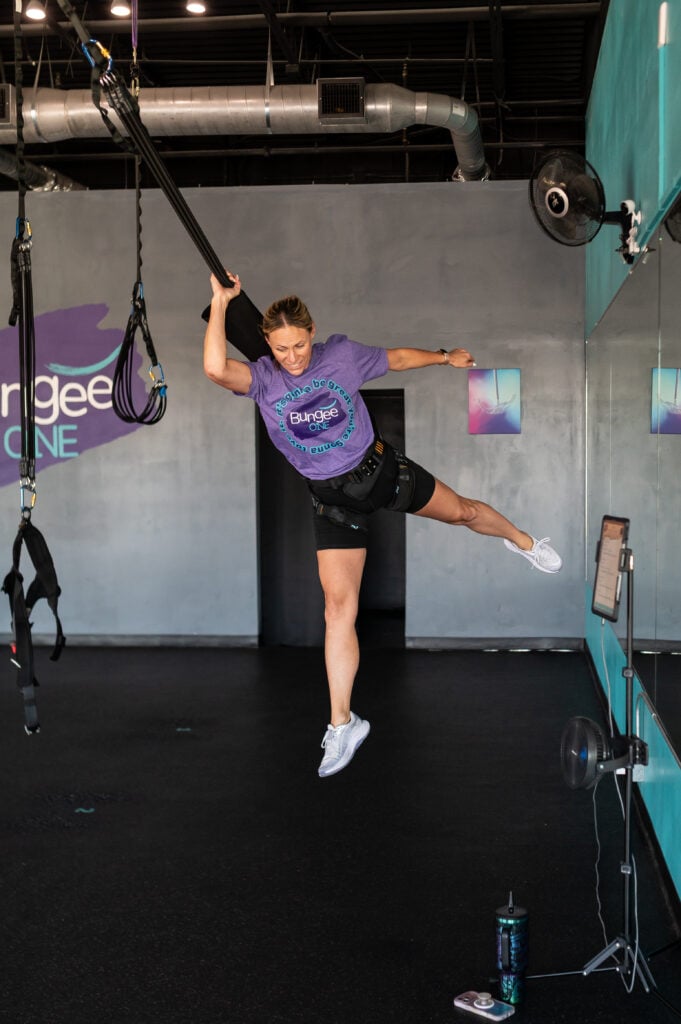 Woman in a purple BungeeONE shirt kicking one leg out while airborne