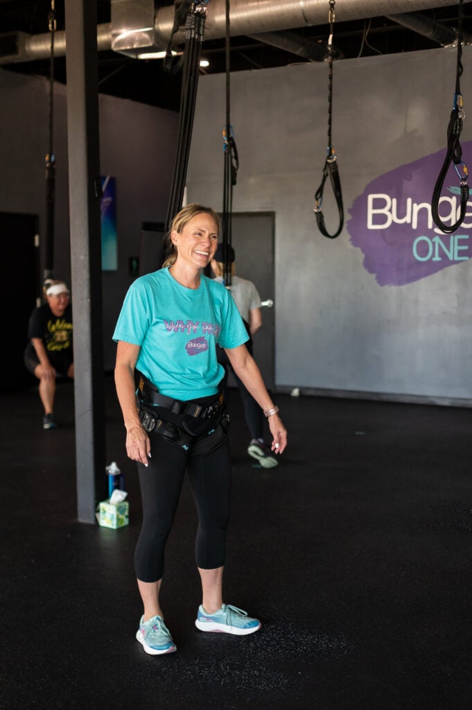 Smiling woman in a teal shirt standing in a bungee harness